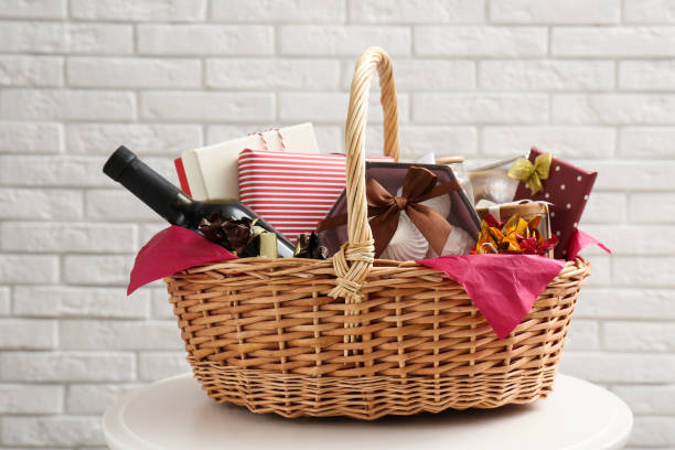 Wicker gift basket with bottle of wine on table near white brick wall